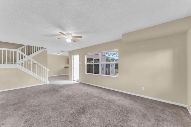 empty room with a textured ceiling, carpet flooring, a ceiling fan, baseboards, and stairs