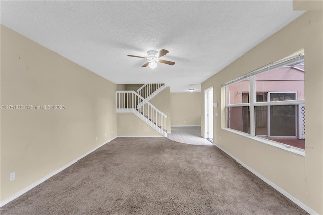 carpeted empty room featuring a ceiling fan, baseboards, stairway, and a textured ceiling