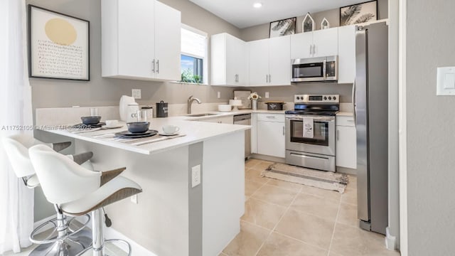 kitchen featuring stainless steel appliances, white cabinets, light countertops, and a breakfast bar area