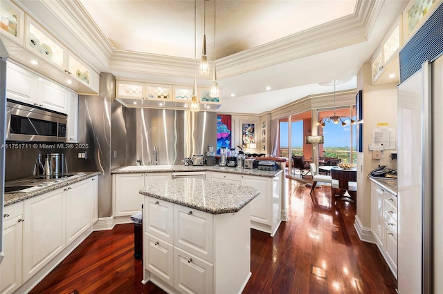 kitchen featuring a kitchen island, appliances with stainless steel finishes, glass insert cabinets, hanging light fixtures, and a peninsula