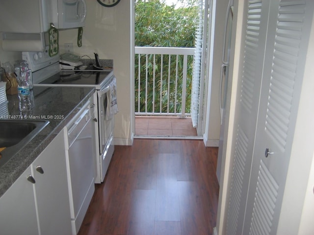 kitchen featuring dark wood-style floors, white appliances, a sink, and baseboards