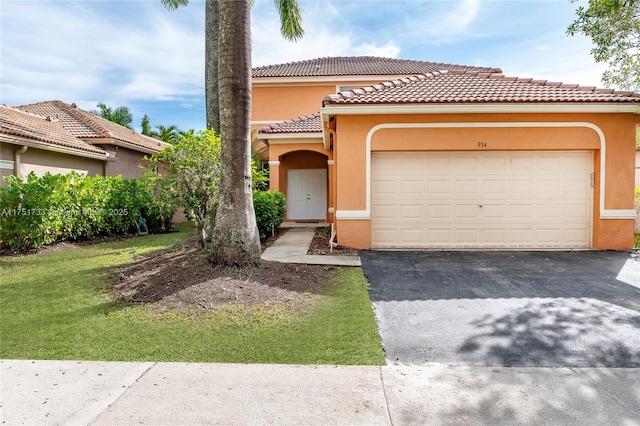 mediterranean / spanish home featuring an attached garage, a tiled roof, aphalt driveway, and stucco siding