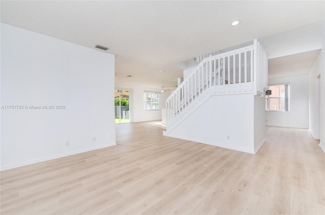 unfurnished living room featuring light wood-style floors, a ceiling fan, visible vents, stairs, and baseboards