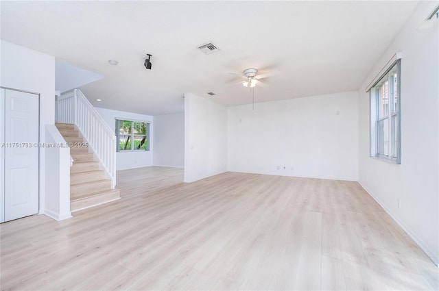 unfurnished living room featuring visible vents, baseboards, light wood-type flooring, a ceiling fan, and stairway
