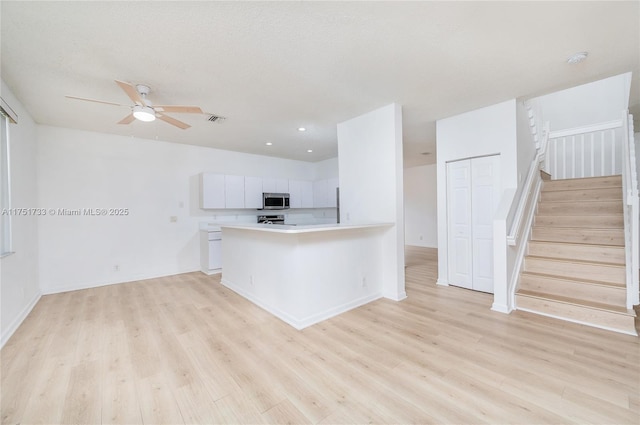 kitchen with stainless steel microwave, light wood-style flooring, light countertops, white cabinets, and visible vents