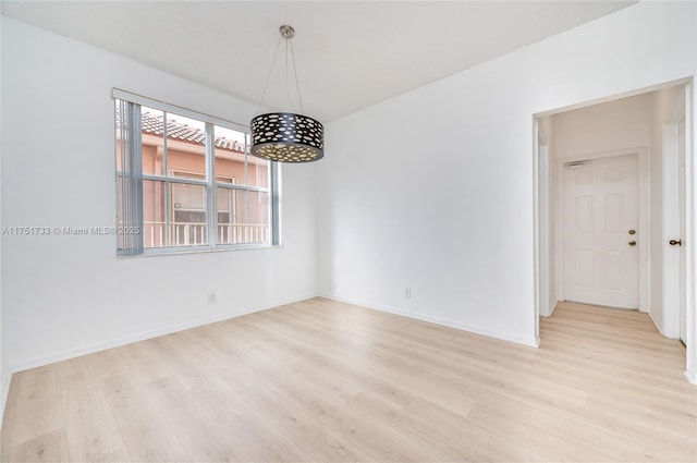 spare room featuring light wood-style flooring, a notable chandelier, and baseboards