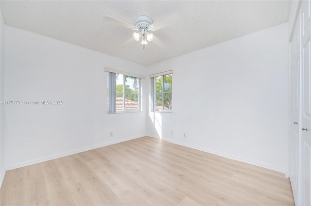 empty room featuring light wood-style flooring, ceiling fan, baseboards, and a textured ceiling