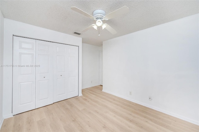 unfurnished bedroom featuring light wood-style flooring, a textured ceiling, a closet, visible vents, and baseboards