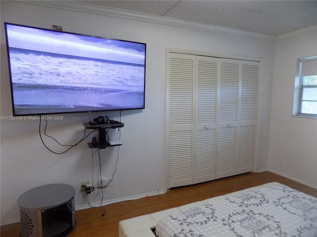 bedroom featuring a closet, baseboards, crown molding, and wood finished floors