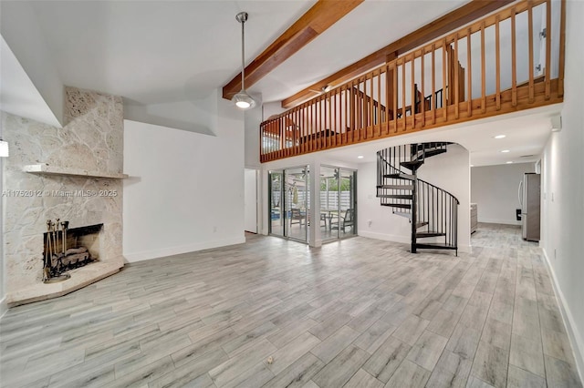 unfurnished living room with beam ceiling, a large fireplace, wood finished floors, baseboards, and stairs