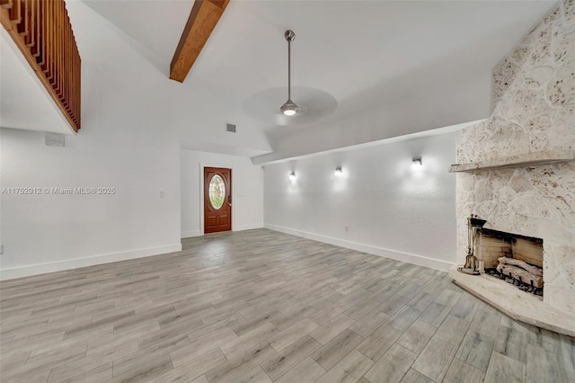 unfurnished living room with ceiling fan, a stone fireplace, light wood-style flooring, visible vents, and beam ceiling