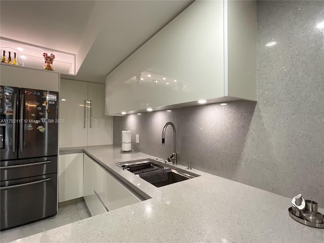 kitchen featuring decorative backsplash, freestanding refrigerator, white cabinetry, a sink, and modern cabinets