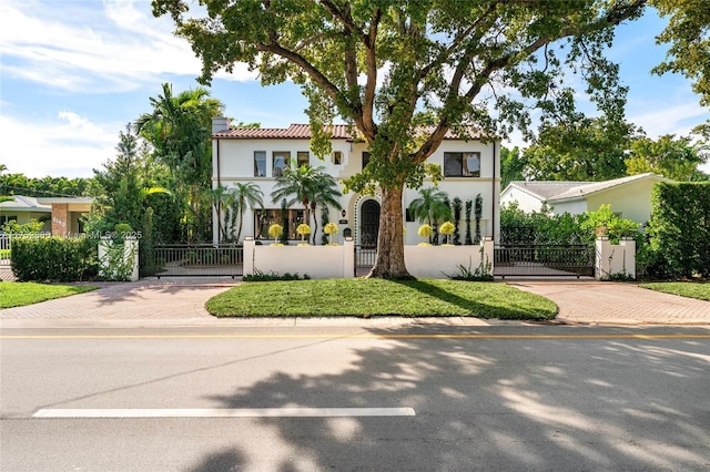 mediterranean / spanish home with a fenced front yard, a gate, a chimney, and stucco siding