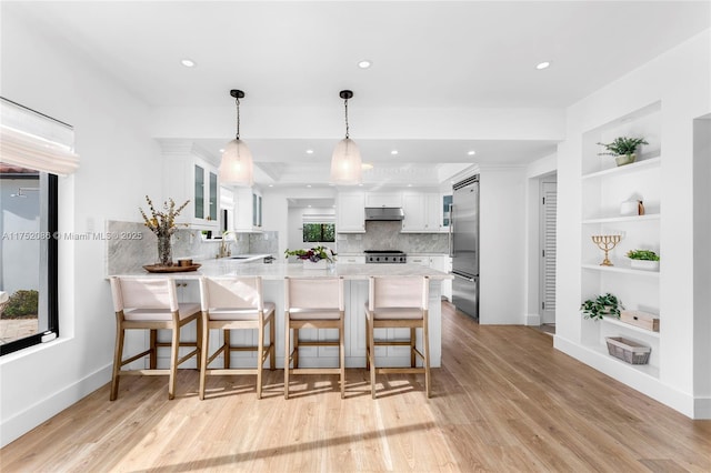 kitchen with built in fridge, a peninsula, stove, white cabinetry, and a kitchen bar