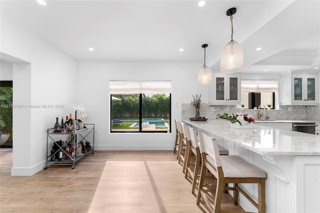 kitchen featuring light stone counters, white cabinets, hanging light fixtures, plenty of natural light, and glass insert cabinets