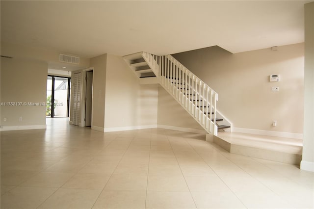 tiled spare room with visible vents, stairway, and baseboards