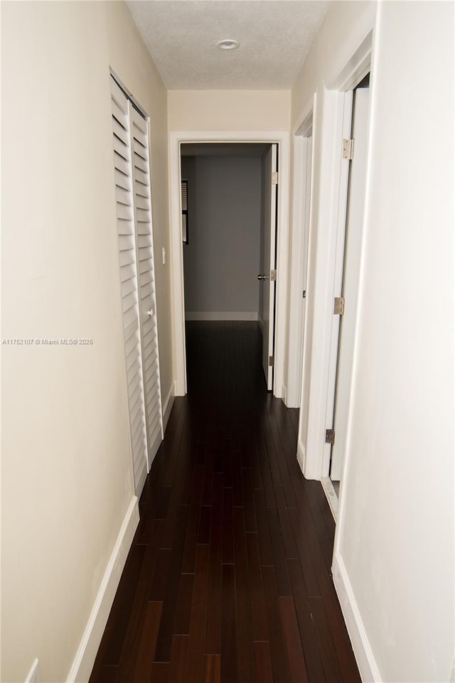 hallway featuring dark wood-style flooring, a textured ceiling, and baseboards