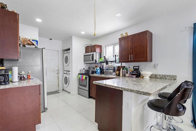 kitchen with a kitchen breakfast bar, a textured ceiling, stacked washing maching and dryer, appliances with stainless steel finishes, and a peninsula