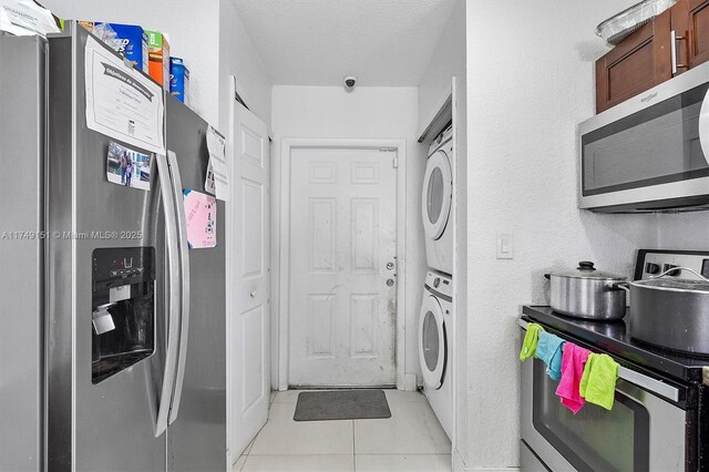 clothes washing area with a textured ceiling, stacked washer / dryer, light tile patterned floors, laundry area, and a textured wall