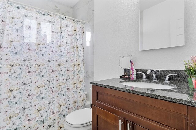 full bathroom with vanity, toilet, and a textured wall