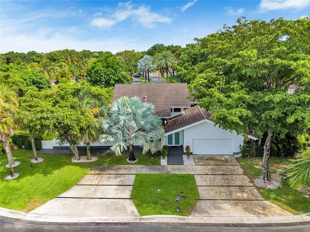 view of property hidden behind natural elements with driveway, a tiled roof, an attached garage, a front lawn, and stucco siding