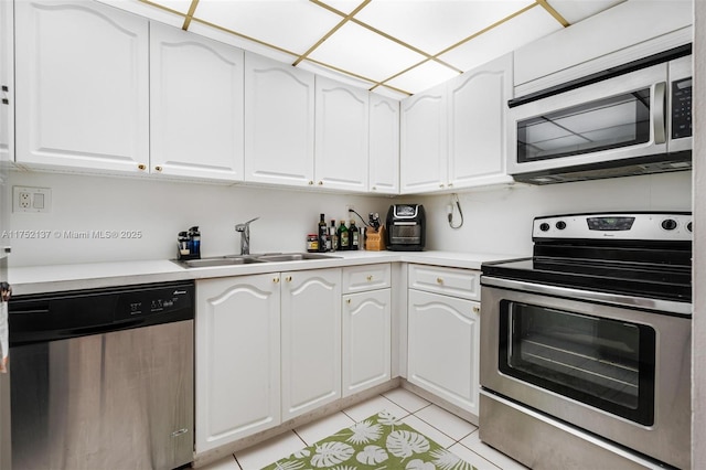 kitchen with light tile patterned floors, appliances with stainless steel finishes, light countertops, white cabinetry, and a sink