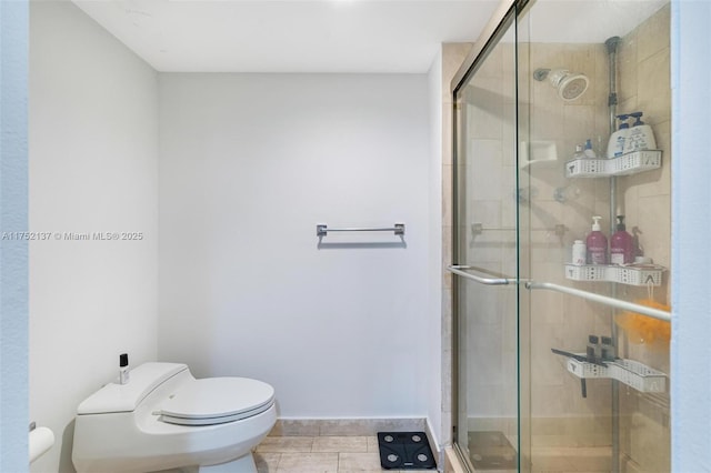 bathroom featuring toilet, a shower stall, baseboards, and tile patterned flooring