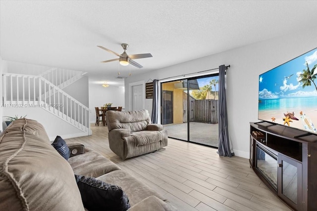 living room with light wood finished floors, ceiling fan, a textured ceiling, baseboards, and stairs