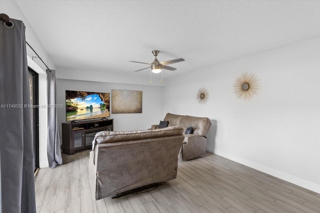 living area with a ceiling fan, light wood-style flooring, baseboards, and a textured ceiling