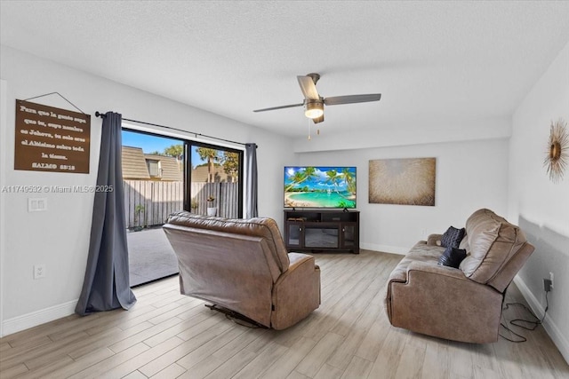 living area with light wood-type flooring, ceiling fan, a textured ceiling, and baseboards