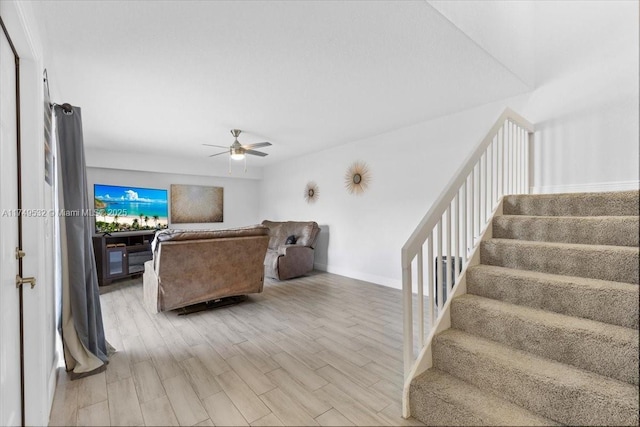 living room featuring light wood finished floors, stairs, baseboards, and a ceiling fan