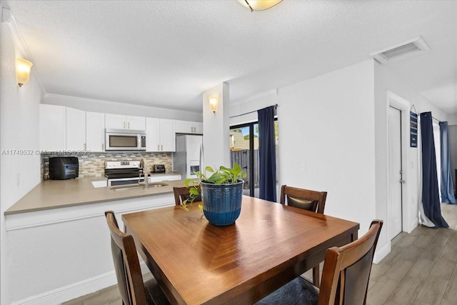 dining area with light wood-type flooring, visible vents, and a textured ceiling