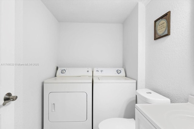 washroom featuring a textured wall, laundry area, and separate washer and dryer