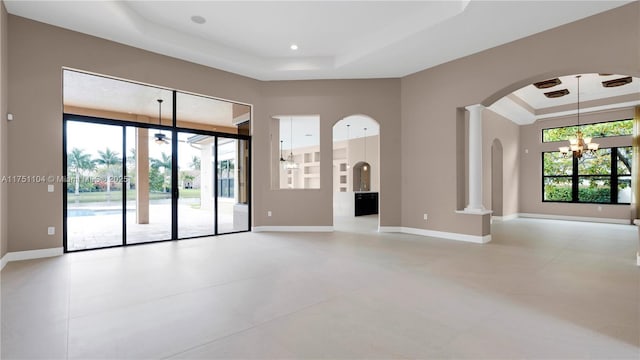 unfurnished room featuring decorative columns, baseboards, a raised ceiling, arched walkways, and an inviting chandelier