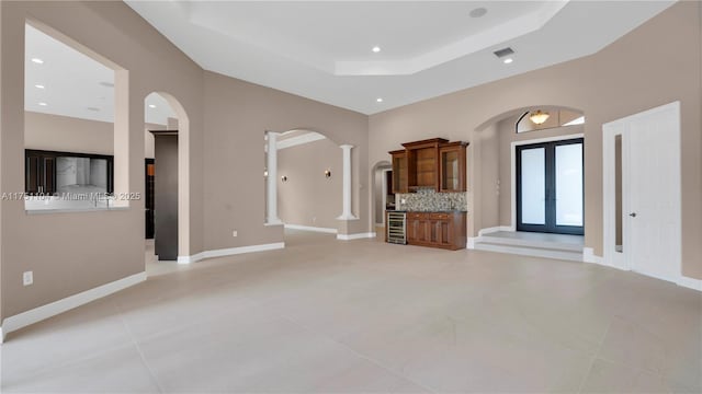 unfurnished living room with arched walkways, french doors, wine cooler, decorative columns, and a raised ceiling