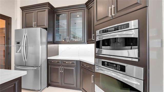 kitchen featuring appliances with stainless steel finishes, dark brown cabinetry, glass insert cabinets, and decorative backsplash