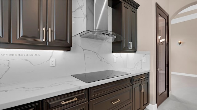 kitchen with light stone counters, black electric stovetop, tasteful backsplash, dark brown cabinetry, and wall chimney range hood