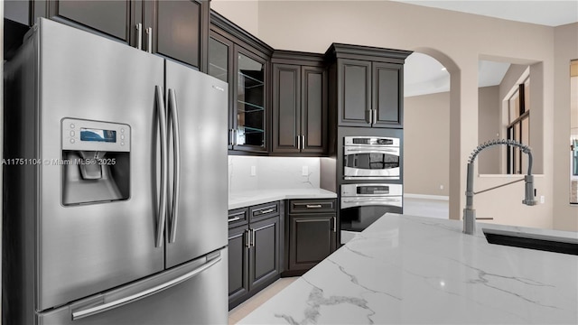 kitchen featuring light stone countertops, dark brown cabinetry, glass insert cabinets, and stainless steel appliances