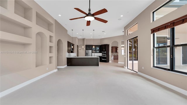 unfurnished living room with baseboards, built in features, arched walkways, and recessed lighting