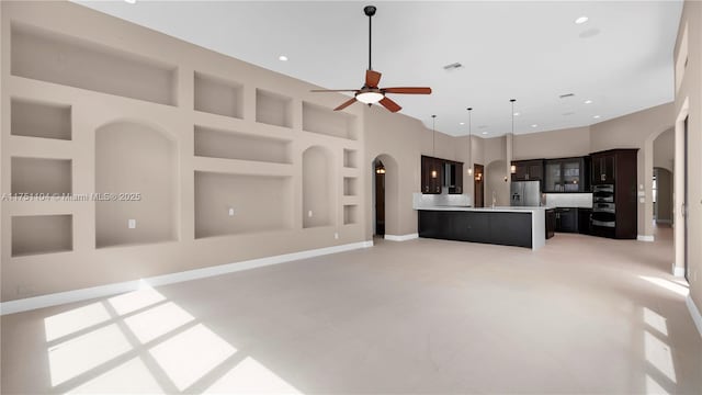 unfurnished living room featuring built in shelves, arched walkways, visible vents, a towering ceiling, and a ceiling fan