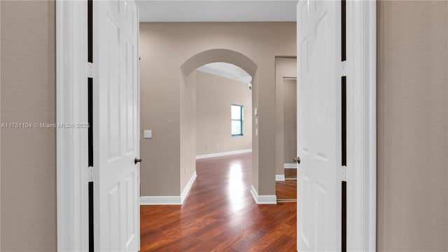 hallway with dark wood-style floors, baseboards, and arched walkways