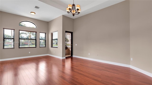 empty room with dark wood-type flooring, visible vents, a notable chandelier, and baseboards