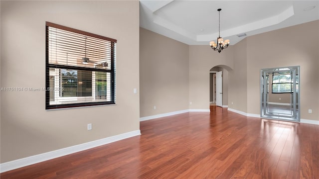 unfurnished room with arched walkways, a raised ceiling, baseboards, and wood finished floors