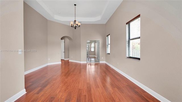 unfurnished room with arched walkways, a raised ceiling, an inviting chandelier, wood finished floors, and baseboards