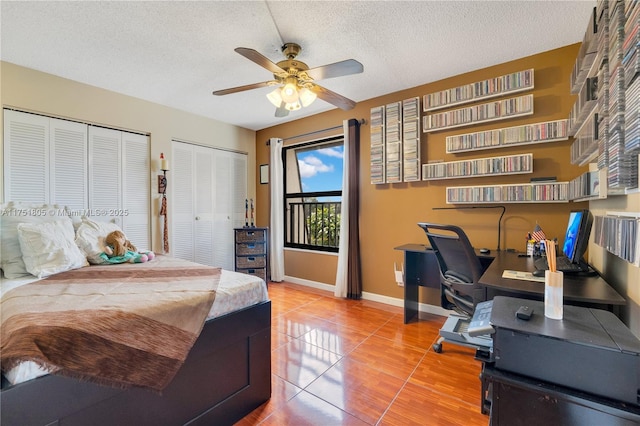 tiled bedroom with ceiling fan, a textured ceiling, baseboards, and two closets