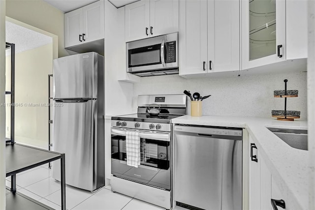 kitchen with stainless steel appliances, light stone counters, glass insert cabinets, and white cabinets