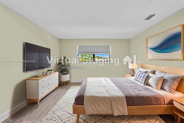 bedroom featuring visible vents, baseboards, a textured ceiling, and light wood finished floors