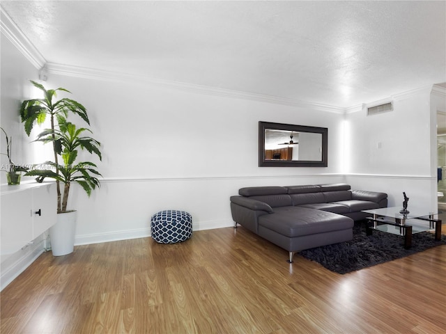 living area with ornamental molding, wood finished floors, visible vents, and baseboards