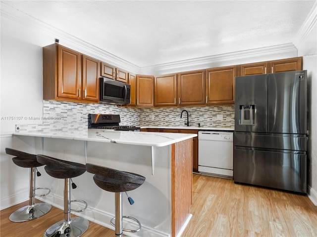 kitchen featuring brown cabinetry, light wood-style flooring, appliances with stainless steel finishes, ornamental molding, and a peninsula