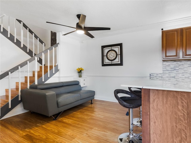 living area featuring light wood finished floors, stairs, baseboards, and crown molding